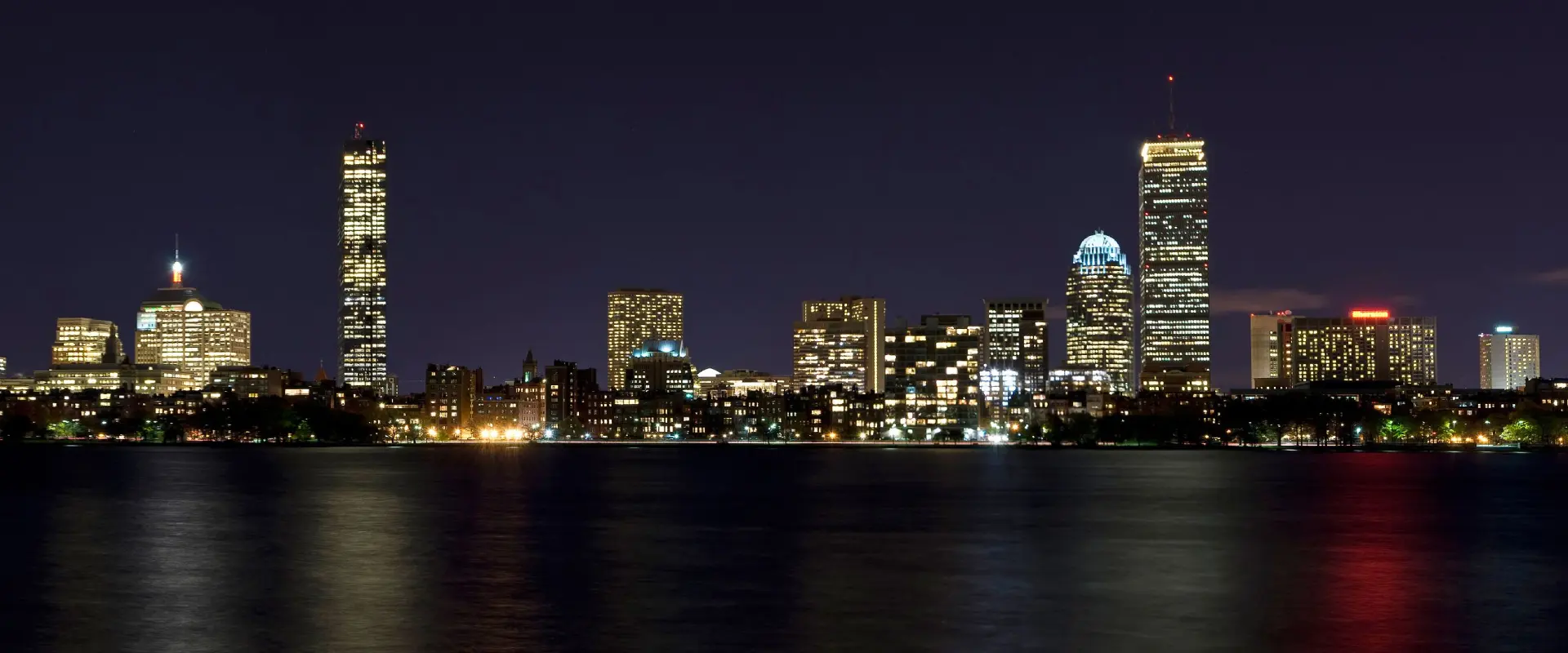 A city skyline at night with lights reflecting on the water.