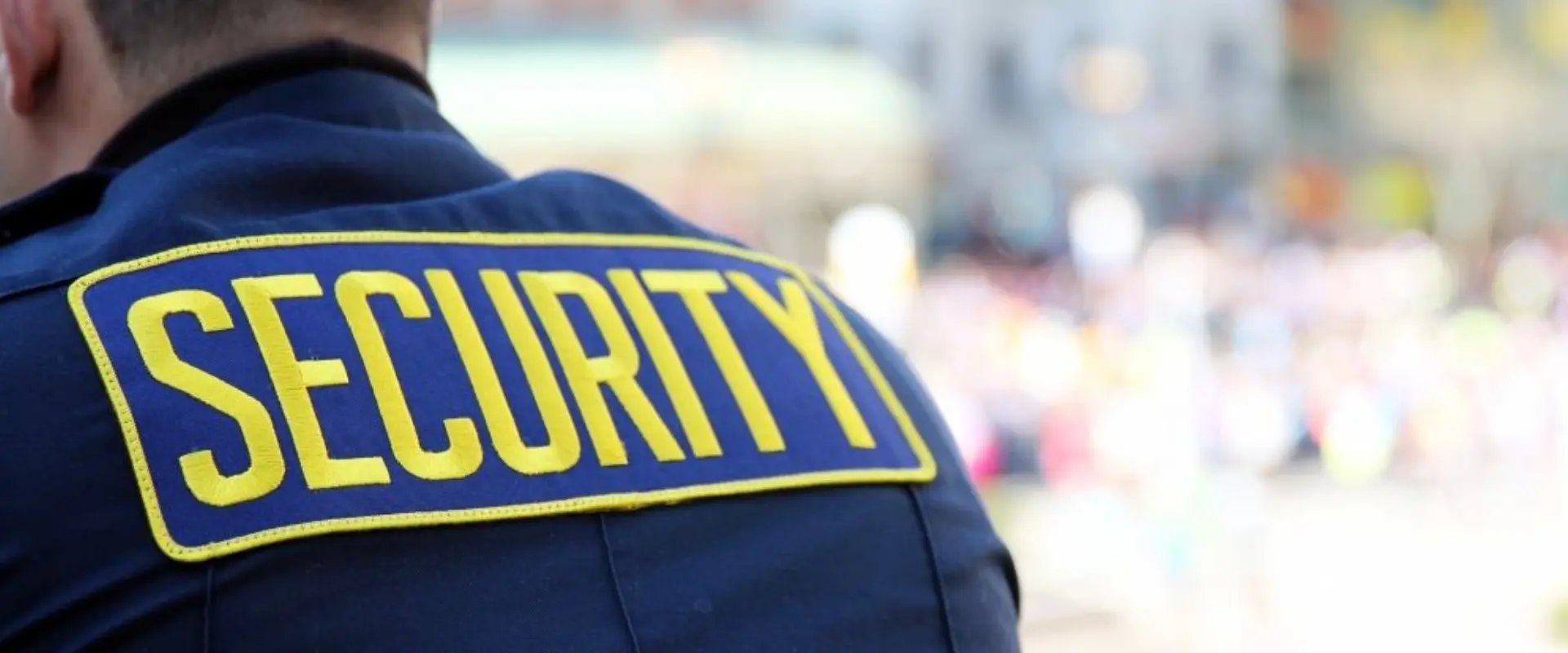 A security guard is wearing his uniform and has the word " security " on it.