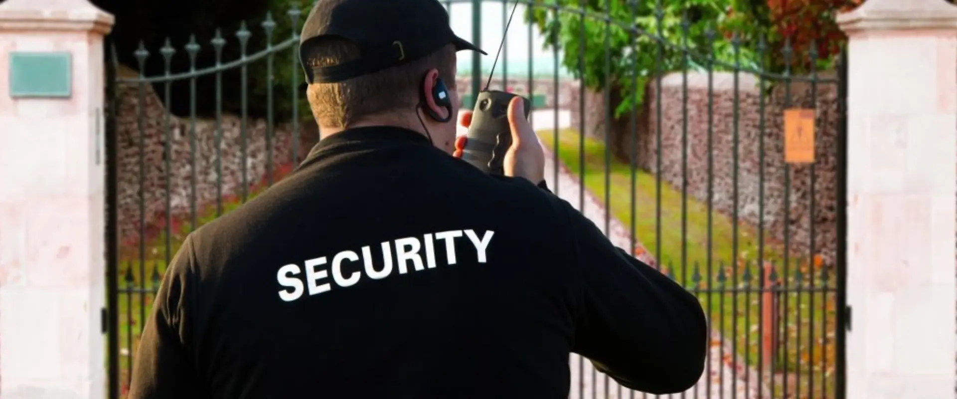 A security guard is standing behind the fence.